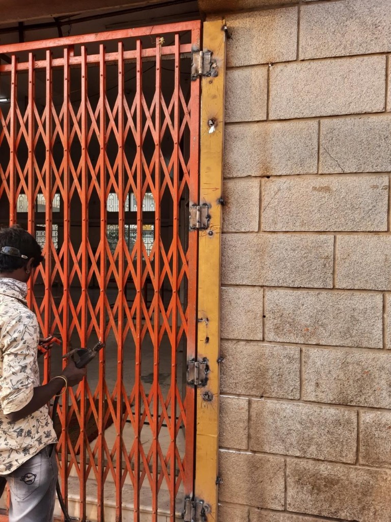Worker Welding and Painting Red Collapsible Security Gate