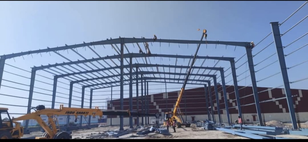 Pre-Engineered Building steel portal framework erection using a heavy-duty yellow crane on site