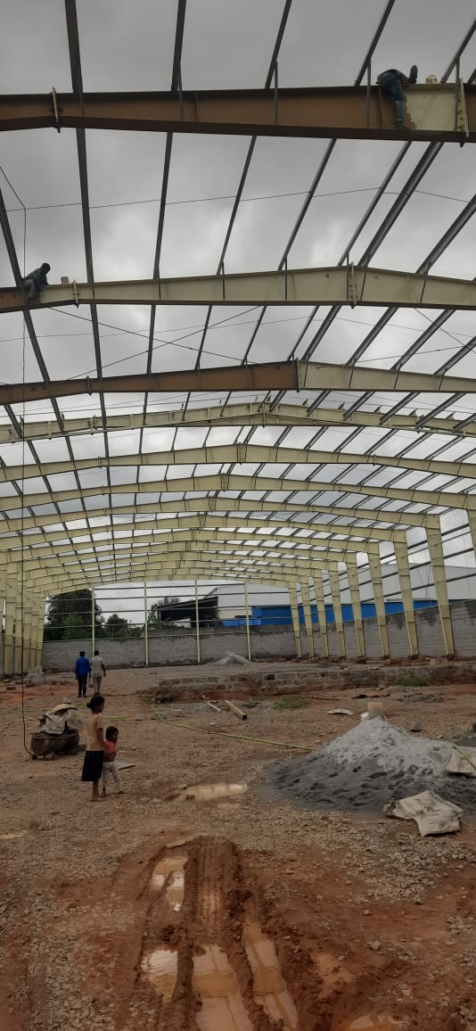 Workers securing steel trusses on a pre-engineered building portal framework high above ground