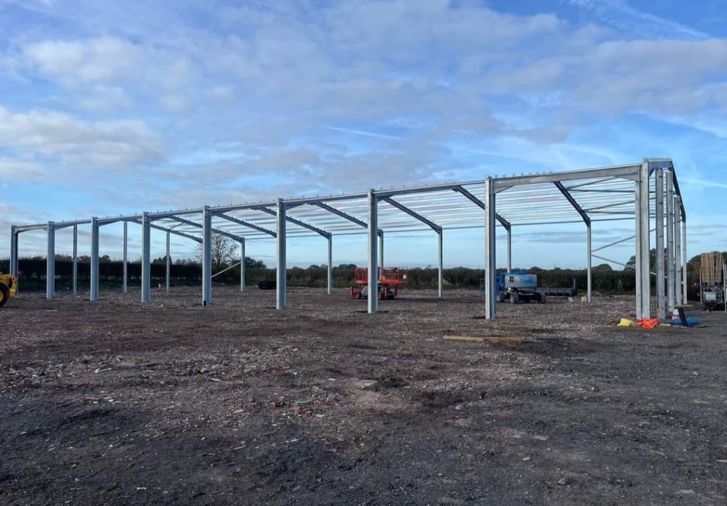 Pre-Engineered Building steel frame erection on gravel foundation under cloudy sky with cherry picker lifts inside