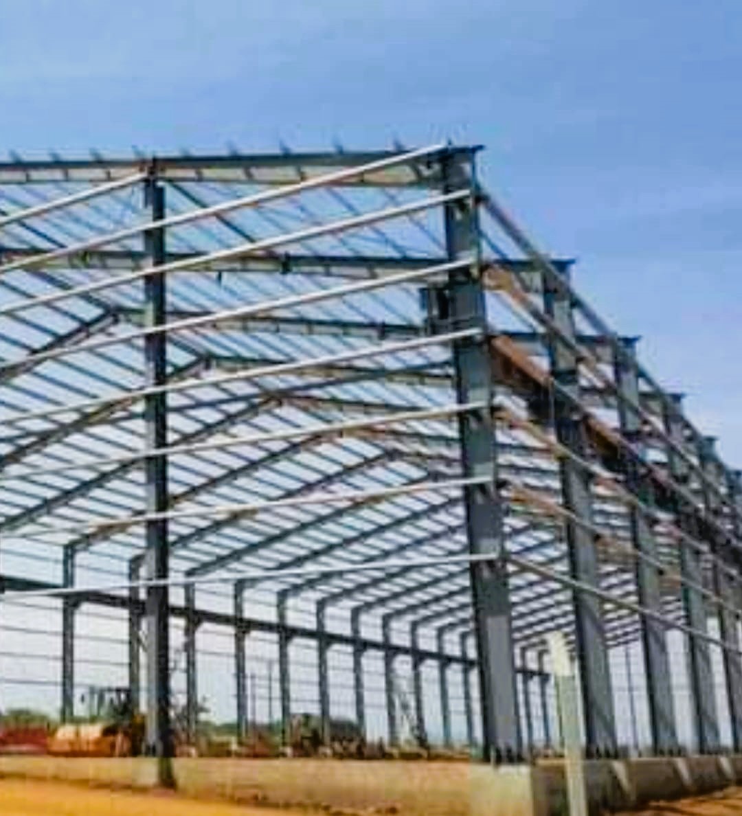 Completed structural steel portal frames of a large warehouse building showing cross bracing and purlins