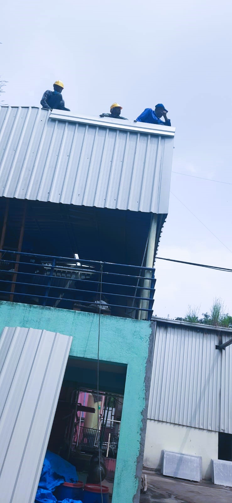 Construction workers installing corrugated steel roofing sheets on warehouse structure