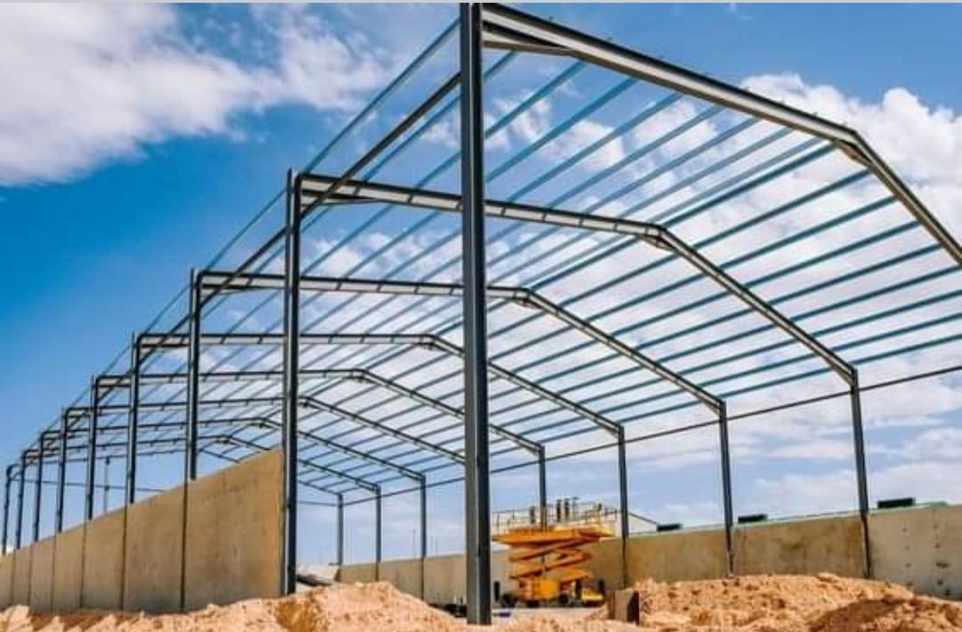 Erecting steel framework of a large industrial warehouse building using a yellow scissor lift